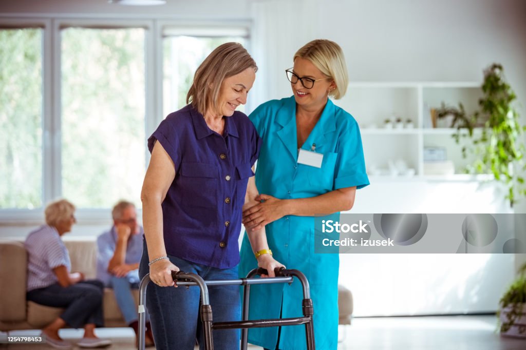 Cheerful nurse helping senior woman to use walking frame People in nursing home. Friendly nurse wearing uniform helping elderly lady to use walking frame. Assistance Stock Photo