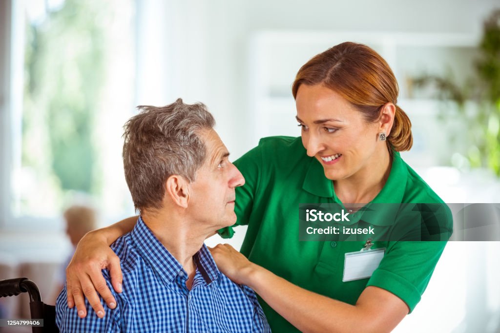 Cheerful social worker supporting senior man Elderly man in retirement home. Friendly nurse talking with worried senior man sitting in wheelchair. Senior Men Stock Photo