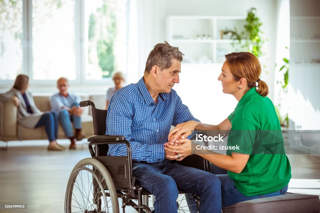 Female social worker consoling senior man Elderly man in retirement home. Friendly nurse talking with worried senior man sitting in wheelchair. 70-79 Years Stock Photo