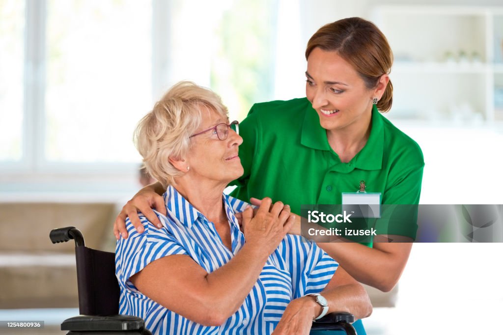Female social worker supporting senior woman Elderly lady in retirement home. Friendly nurse talking with senior woman, sitting in wheelchair. Assisted Living Stock Photo
