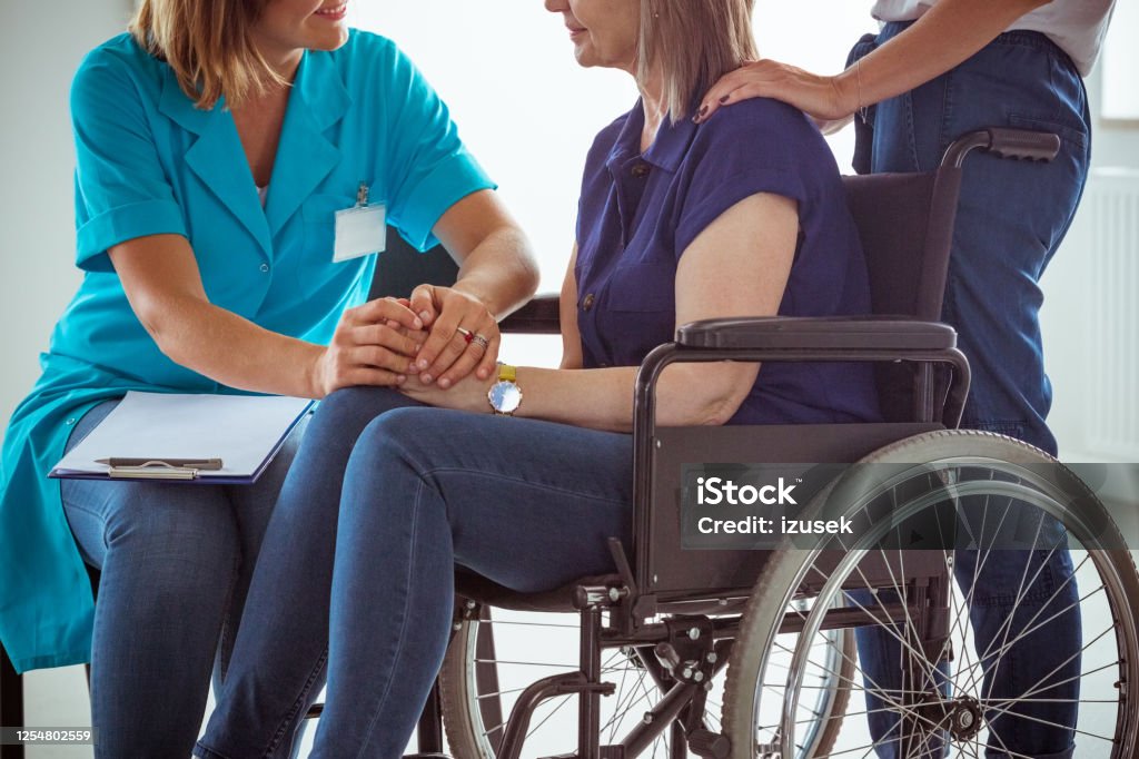 Nurse talking with worried senior woman in hospital waiting room Nurse and elderly lady discussing medical test results. Senior woman sitting in wheelchair, social worker assisting her. 70-79 Years Stock Photo