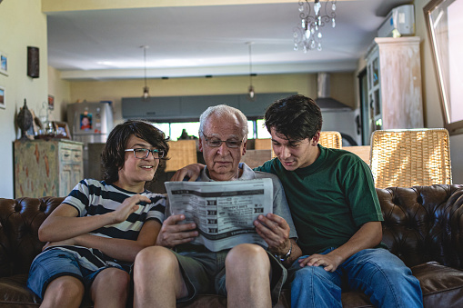Young boys reading newspaper with their senior adult grandfather in the living room