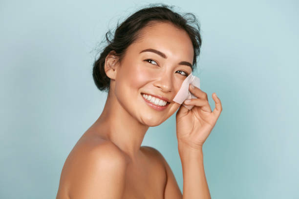 Face skin care. Smiling woman using oil blotting paper portrait Face skin care. Smiling woman using facial oil blotting paper portrait. Closeup of beautiful happy asian girl model with natural makeup using oil absorbing sheets, beauty product at studio stage makeup women beauty human face stock pictures, royalty-free photos & images