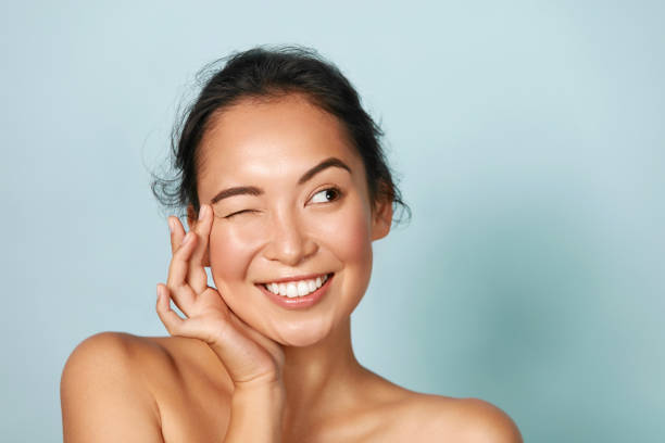 Skin care. Woman with beauty face touching facial skin portrait Skin care. Woman with beauty face touching healthy facial skin portrait. Beautiful smiling asian girl model with natural makeup touching glowing hydrated skin on blue background closeup wrinkled stock pictures, royalty-free photos & images
