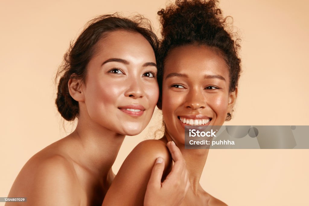 Beauty. Smiling women with perfect face skin and makeup portrait Beauty. Smiling women with perfect face skin and natural makeup portrait. Beautiful happy asian and african girl models with different types of skin on beige background. Spa skin care concept Women Stock Photo