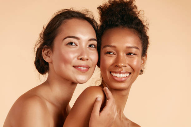 Beauty. Smiling women with perfect face skin and makeup portrait Beauty. Smiling women with perfect face skin and natural makeup portrait. Beautiful happy asian and african girl models with different types of skin on beige background. Spa skin care concept glowing stock pictures, royalty-free photos & images