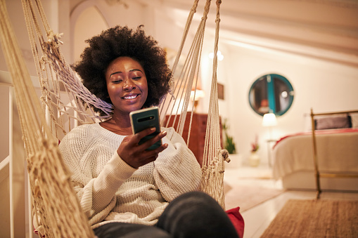Young African American woman text messaging on her phone while relaxing at home during social distance measures