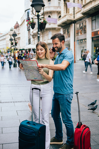 Tourists with luggage holding a map and talking on a phone for an information