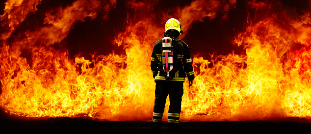 Rear of firefighter with fire uniform and equipment on flame background. Panoramic with copy space