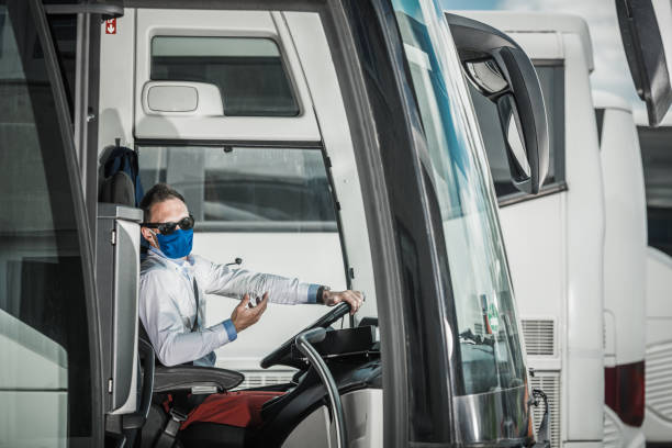 Coach Bus Driver Operating Vehicle. Professional Male Driver With Protective Face Mask Driving Coach Bus Out Of Parking Lot. intercity train photos stock pictures, royalty-free photos & images