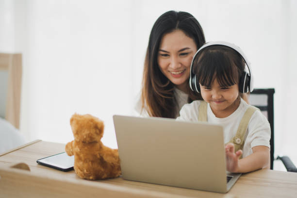 love of young asian mother and daughter learning online by computer laptop in living room at home which smiling and felling happy. daughter use headphone. asian love family live at home concept. - baby animals audio imagens e fotografias de stock
