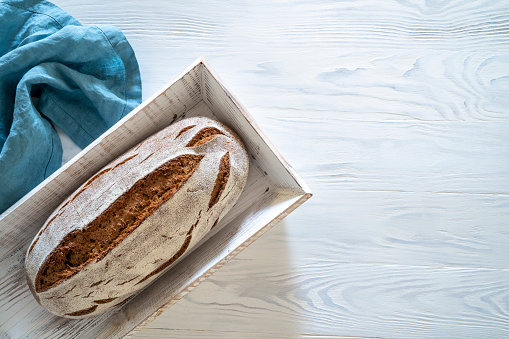 Wholegrain rye bread loaf on white wooden background in white wood tray