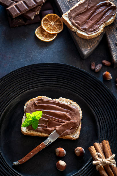 istock Chocolate cream spread on bread slice and hazelnuts on a dark black plate 1254822589