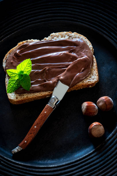 istock Chocolate cream spread on bread slice and hazelnuts on a dark black plate 1254822763