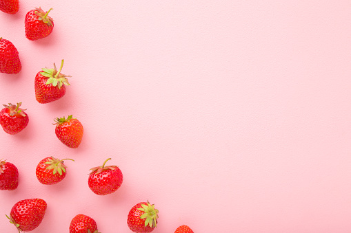 Red bright strawberries on light pink table background. Beautiful fresh berries. Pastel color. Flat lay. Empty place for text. Top down view.