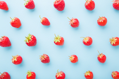 Red bright strawberries on light blue table background. Beautiful fresh berries pattern. Pastel color. Closeup. Flat lay. Top down view.