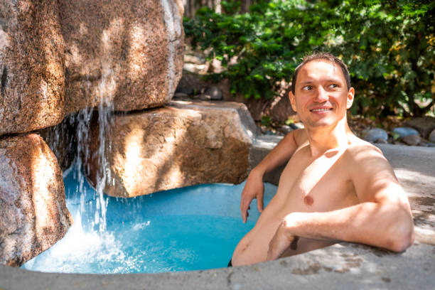 joven hombre sonriente feliz nadando en el balneario japonés por la piscina de piedra colorida agua azul y cascada en japón onsen - stone wellbeing zen like blue fotografías e imágenes de stock