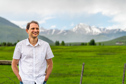 Crested Butte, Colorado near Gunnison countryside with happy man standing by rural fence in summer on cloudy day with green grass and mountain view