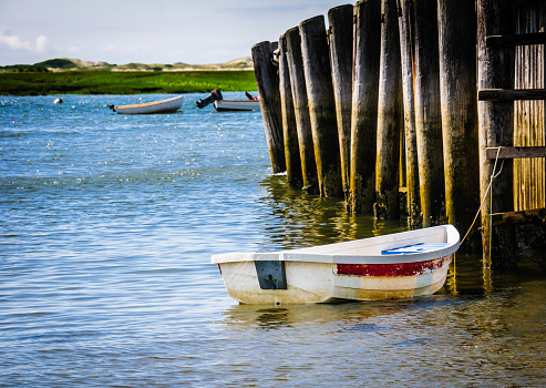 A small white rowboat is tied to an old dock on Cape Cod.
