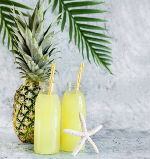 istock Pineapple juice in glass bottles with straws and pineapple fruit on blue marble background. 1254840372