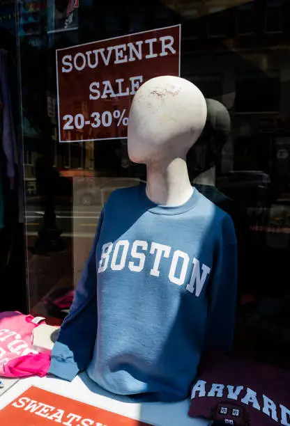 Tourist souvenir store display window advertising 20 - 30% discount on merchandise. Outdoor display table with mannequin torso wearing blue Boston sweatshirt and with other souvenir clothing.