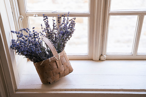 Bouquet of blossoming lavender flowers in a basket put on the window of a rustic house.
