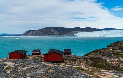 Greenland glacier nature landscape with famous Eqi glacier and lodge cabins. Tourist destination Eqi glacier in West Greenland AKA Ilulissat and Jakobshavn Glacier. Heavlly affected by Climate Change.