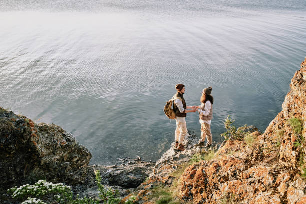 istock Young affectionate romantic couple holding by hands while standing by waterside 1254844345
