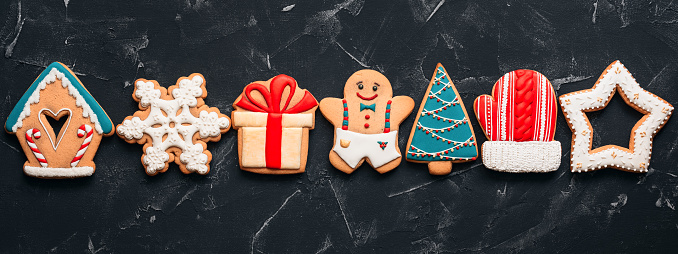 Christmas various colored gingerbread cookies in a line on a black stone background, banner. Top view, flat lay, border