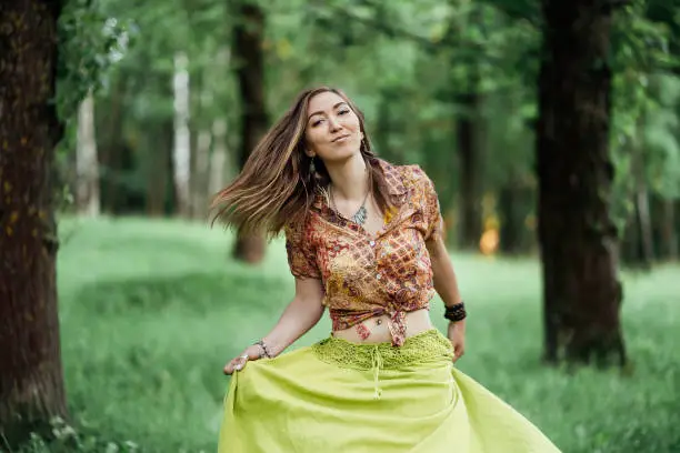 Beautiful young woman wearing bohostyle clothes posing in the rays of the evening sun, sunset. Boho style fashion, female wearing silver jewelry having fun in park outdoors