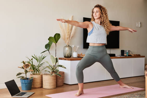 Go with the yoga flow Shot of a young woman practicing her yoga routine at home warrior 2 stock pictures, royalty-free photos & images