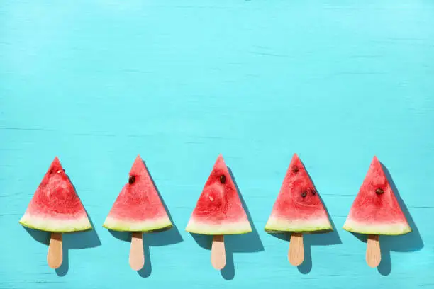 Photo of Watermelon slice popsicles on a blue color background