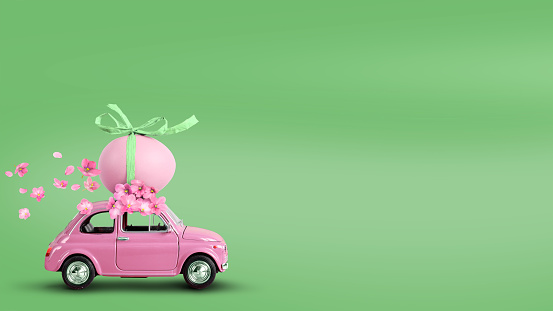 Pink toy car carrying an easter egg on the roof on a green background.