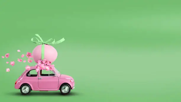 Photo of Pink toy car carrying an easter egg on the roof on a green background.