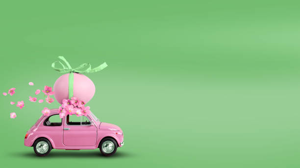 carro de brinquedo rosa carregando um ovo de páscoa no telhado em um fundo verde. - easter egg fotos - fotografias e filmes do acervo