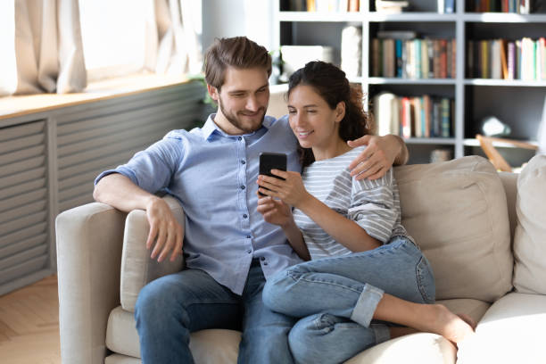 istock Happy young couple using smartphone together, relaxing on couch 1254860345