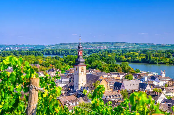 Aerial view of Rudesheim am Rhein historical town centre with clock tower spire of St. Jakobus catholic church and Rhine river, blue sky background, Rhineland-Palatinate and Hesse states, Germany