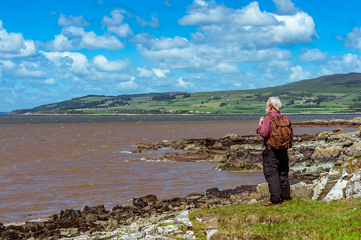 One retired man sitting on a rock at the coast on a sunny windy day.
The location is in Dumfries and Galloway, south west Scotland.