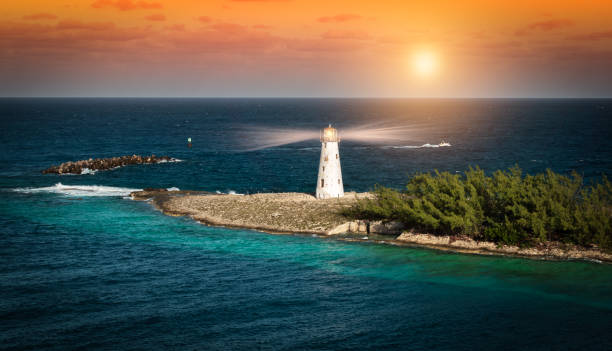 White lighthouse with beams of light on a narrow island at the cruise port of Nassau in the Bahamas. Sunset with orange colored sky on a beautiful summer evening.