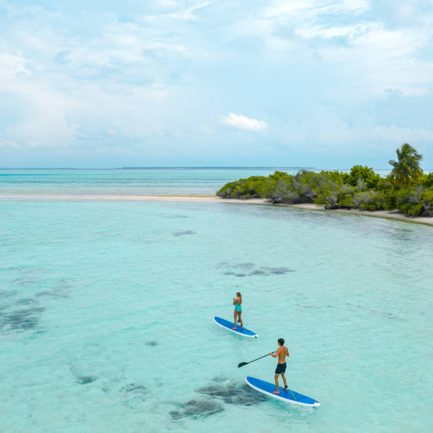 Couple stand up paddle boarding in ocean, Maldives