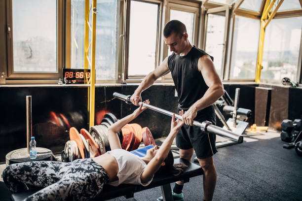 male personal trainer assisting a woman in bench press training in gym - weight training weight bench weightlifting men imagens e fotografias de stock