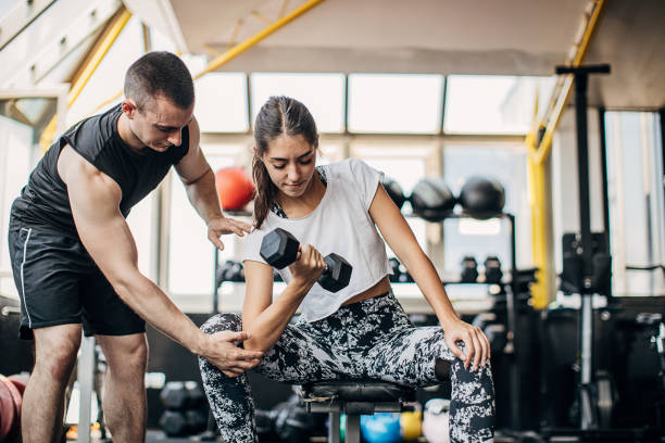 entrenador personal masculino ayudando a una mujer en el entrenamiento de peso en el gimnasio - weight training weight bench weightlifting men fotografías e imágenes de stock