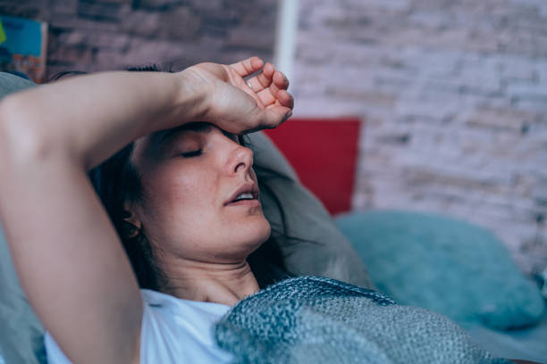 Woman with high fever at home. Sick young woman lying in the bed covered with blanket. Ill woman lying in bed with high temperature. desease stock pictures, royalty-free photos & images