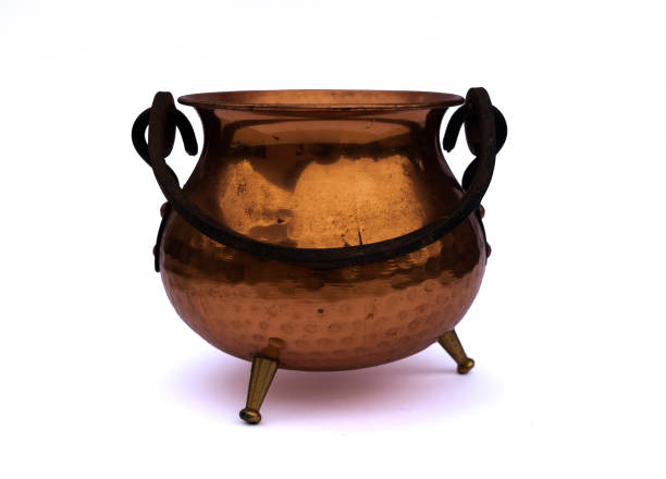 Old antique copper / bronze pot / cauldron / kettle with black holder and three small legs isolated on white studio background