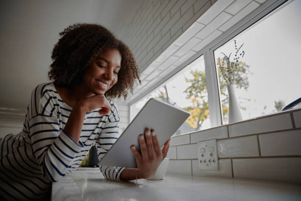 istock Beautiful young woman scrolling or browsing tablet in the kitchen at home checking online recipes 1254870771