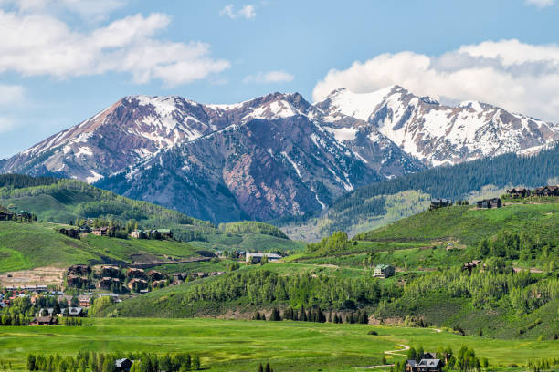 mount crested butte mountain peak range and village in summer with lodging houses on hills with green grass open hill and snowcapped rocky mountains - lodging imagens e fotografias de stock
