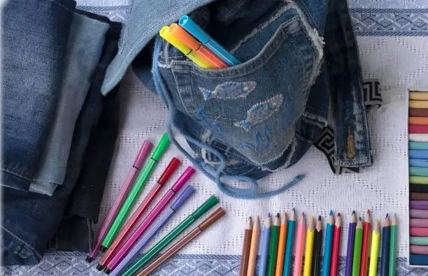 Kids bag from old jeans and colored pencils, crayons and felt-tip pens. Concept of things reuse and back to school handmade.