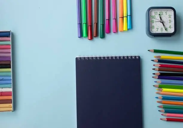Set of school and office supplies on blue  background: pen, clips, note paper, colored pencils, crayons, felt-tip-pens and alarm clock. Concept: back to school. Flatlay, top view.