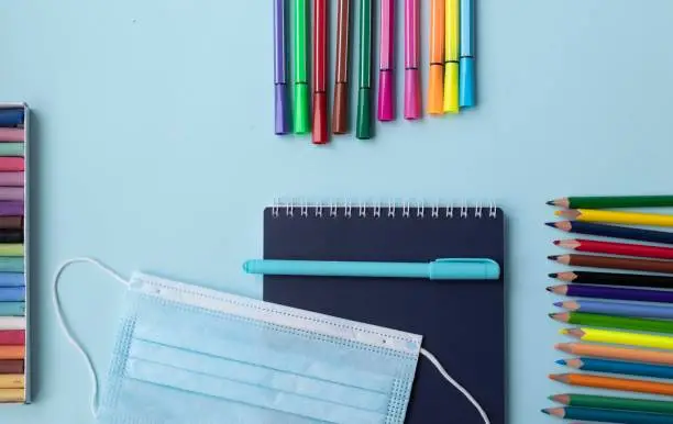 Set of school and office supplies on blue  background: pen, clips, note paper, colored pencils, crayons, felt-tip-pens and alarm clock. Concept: back to school. Flatlay, top view.