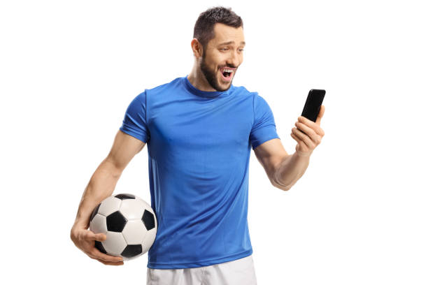 calciatore sorpreso che tiene palla e guarda un cellulare - sports uniform athlete competitive sport professional sport foto e immagini stock